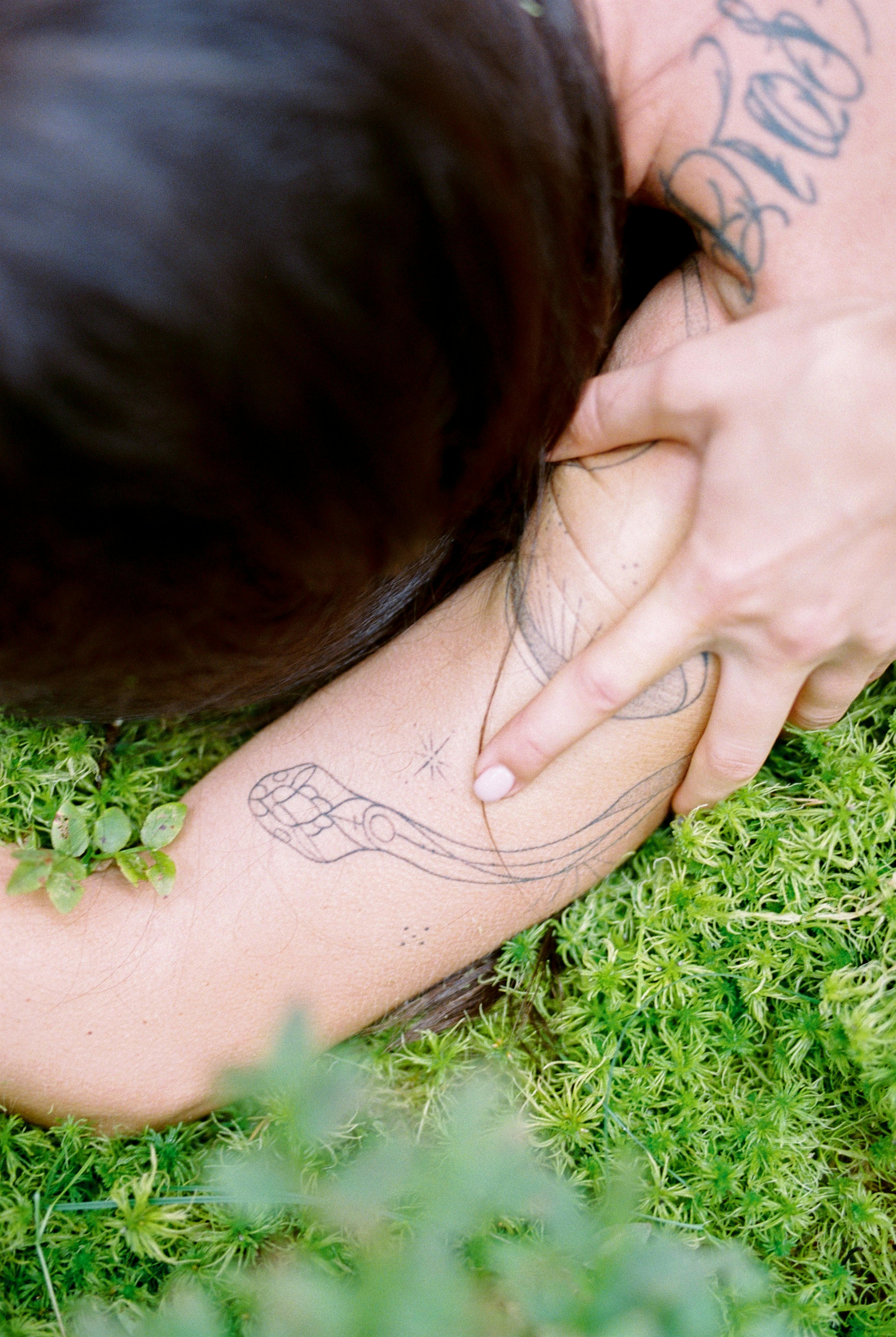 Main posée sur un bras tatoué, dans l'herbe
